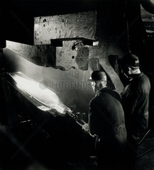 Two workers use a heavy hammer to forge a propellor blade from aluminium.