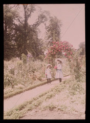 Two girls on a path carrying flowers  1908.
