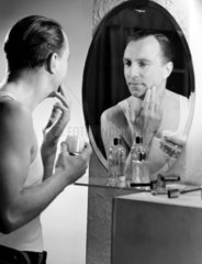 Man applying cream to his face after shaving  c 1950s.