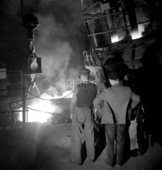 The charging end of a carbon arc furnace  4 men look in to inferno  1951.