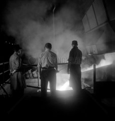 Three steelworkers watching molten steel being poured  1948.