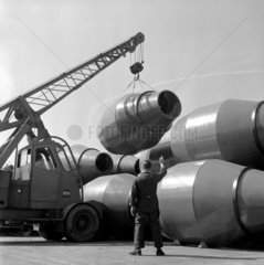 A worker guides a crane lifting a cement mixer barrel from pile  Ransome  1960.