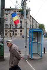 Bukarest  Rumaenien  ein alter Mann geht an der rumaenische Fahne und einem Telefonhaeuschen vorbei