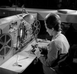 Woman at desk in inspection room splicing reels of 16mm film.