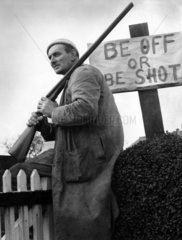 Farmer with gun sitting by 'Be Off or Be Shot' sign  30 November 1967.