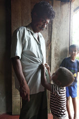 Galle  Sri Lanka  ein Kind hilft seinem behinderten Vater beim zuknoepfen seines Hemdes