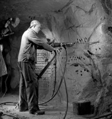 A miner underground bores holes in rock face with drill  Cambourne. 1948.