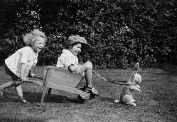 Two children playing with a wheelbarrow harnessed to a toy rabbit  c.1930s.