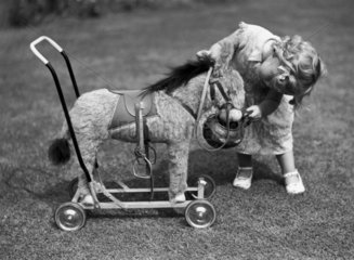 Small child playing with a toy donkey in a garden  c 1920s.