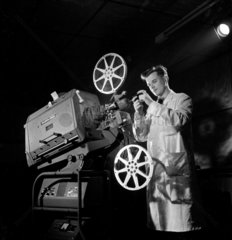 A technician inspects a completed cinema projector  1952.