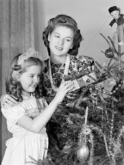 Woman and young girl by a Christmas tree  c 1950.