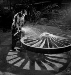 A foundry man burnishes large rail engine wheels after casting  1951.