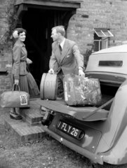 Couple carrying luggage from a car  1950.