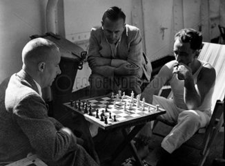 Two men playing chess on a liner as a third