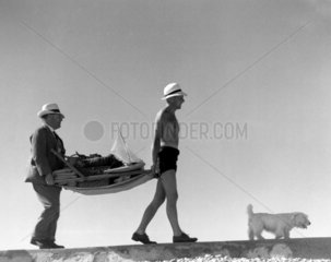 Two men carrying a deckchair laden with hol