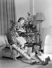Woman putting Christmas presents under the tree  c 1950.