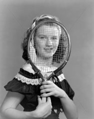 Portrait of a woman looking through a tennis racket  c 1950.