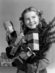 Young girl carrying an armful of Christmas presents  c 1950.