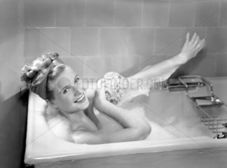 Woman lying in a foam bath washing herself with a sponge  c 1950s.