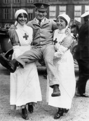 Two female nurses lifting a soldier who was a former patient  1914-1918.