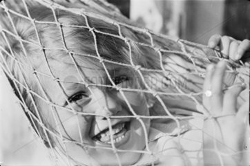 Small child smiling through the netting of a hammock  c.1930s.