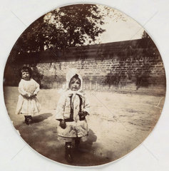 Two small children walking alongside a wall  c 1890s.