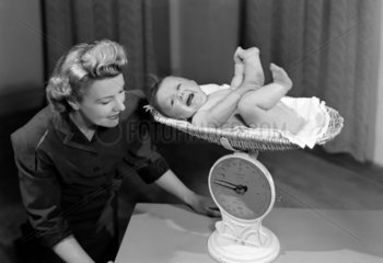 Woman weighing a crying baby on a pair of scales  c 1949.