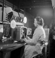 Female technician with headphones testing a 16mm sound projector  1953.