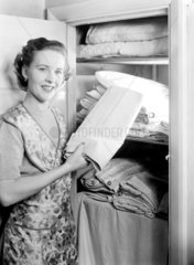 Woman putting laundry away in an airing cupboard  1949.
