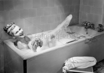 Woman lying in a foam bath with her leg out the water  c 1950s.