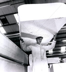 A worker carries a huge slab of polystyrene on his head  1963.