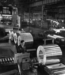 A worker examines finished rolls of aluminium sheets on production line.