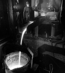 A foundry worker watches molten metal pouring from cupola in to ladle  1962.