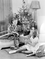 Woman and girl looking at Christmas presents  c 1950.