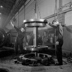 Two men fit a locomotive wheel to steel tyre at the workshops of English Electric.