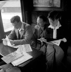 Two men and a boy sitting in a train carriage reading  1950.