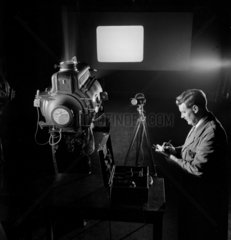 A supervisor measures lamp output using a projector beam with light meter.