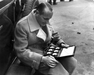 Man sitting on a running board looking at a set of stopwatches  Berlin  1932.
