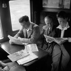 Two men and a boy sitting in a train carriage reading  1950.