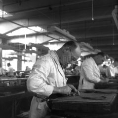 A clicker at work cutting out leather soles at a shoe factory. 1950.