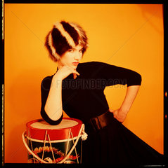 Woman in a fur har  leaning on a drum  1960s.