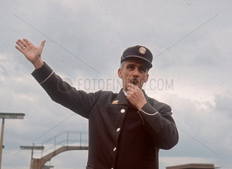 Station guard blowing whistle and signalling to a locomotive  April 1964.