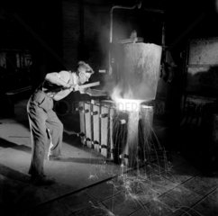 A foundry man makes small ingots with molten metal from an overhead furnace.