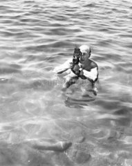 Zoltan Glass taking a photograph standing in the sea  c 1964.