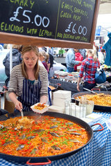 London  Grossbritannien  eine junge Marktfrau verkauft an ihrem Marktstand Paella
