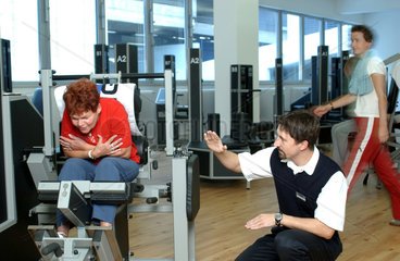 Seniorin an einem Geraet im Fitness-Studio mit Trainer