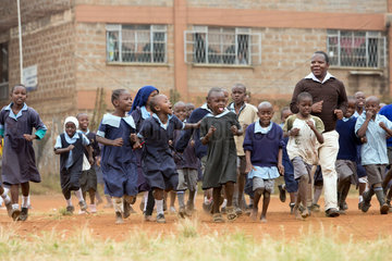 Nairobi  Kenia - Schueler und Schuelerinnen in Schuluniformen laufen mit einem Lehrer auf dem Schulhof des St. John’s Community Centers Pumwani.
