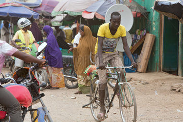 Kakuma  Kenia - Strassenszene mit Menschen  Motorraedern und Fahrrad. Verkehr auf einer belebten unbefestigten Strasse.