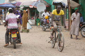 Kakuma  Kenia - Strassenszene mit Menschen  Motorraedern und Fahrrad. Verkehr auf einer belebten unbefestigten Strasse.