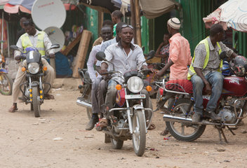 Kakuma  Kenia - Strassenszene mit Menschen und Motorraedern. Motorradverkehr auf einer belebten unbefestigten Strasse.